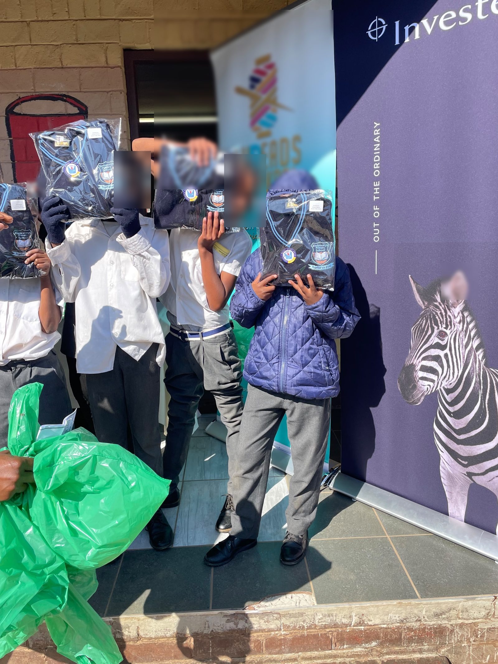Sindawonye Primary School learners holding up their individually labelled school jerseys in front of the Threads for iKasi and Investec banners
