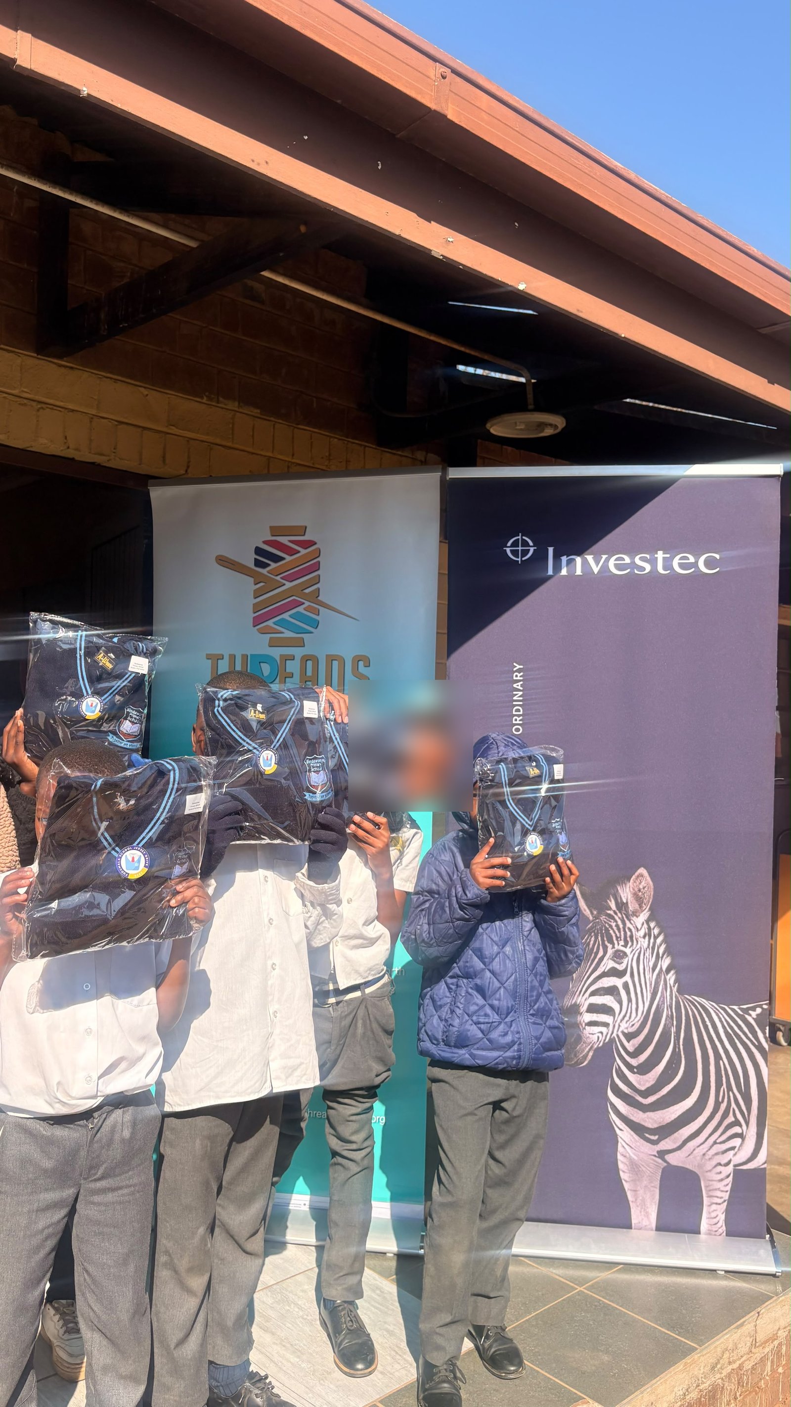 Sindawonye Primary School learners holding up their new school jerseys in front of the Investec banner